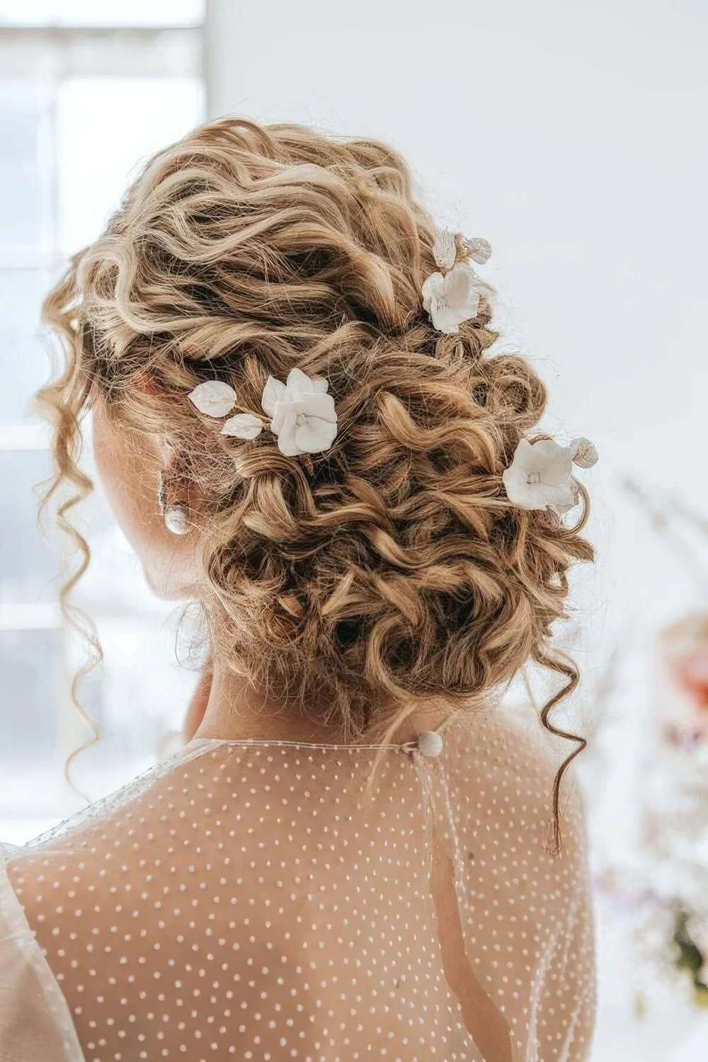 Curly low updo with curls down and some flowers tucked into hair.