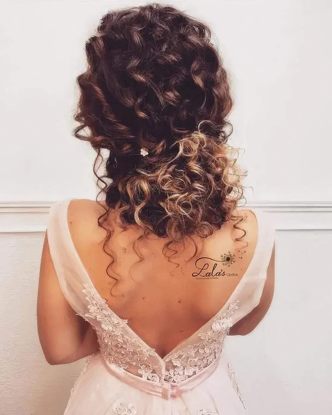 Curly low updo with locks down and twists with a single floral hairpin.