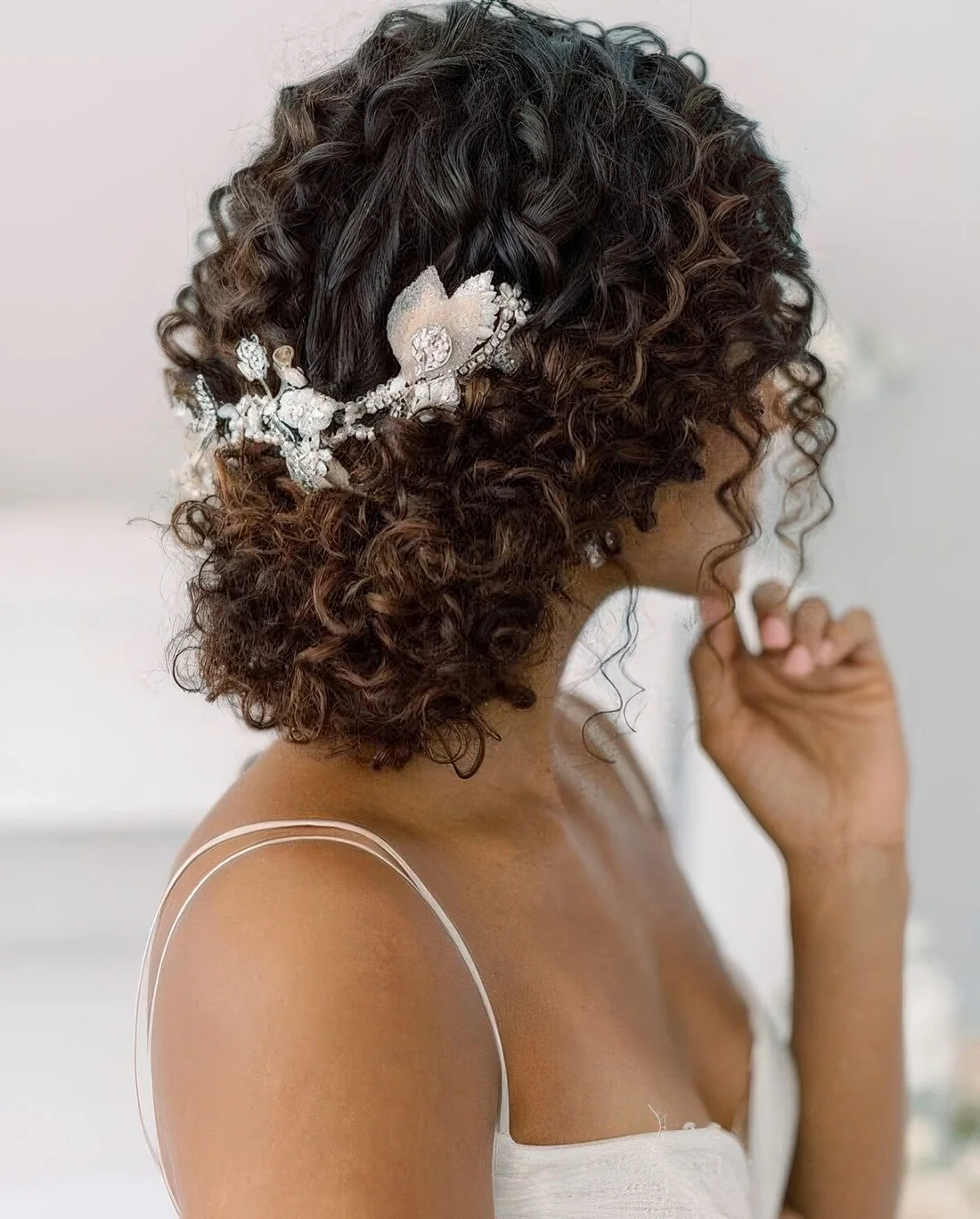 Curly wedding updo with a curly top and a rhinestone and pearl hairpiece.
