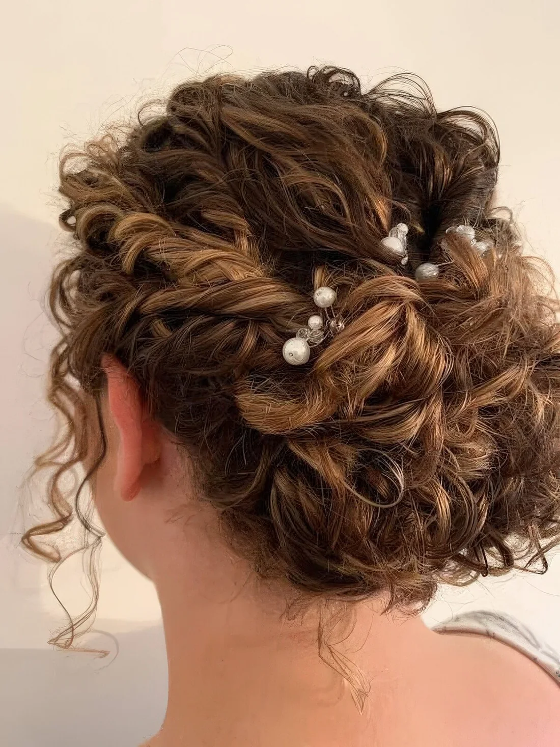Curly wedding updo with tiwsts and curls on top and pearl hair pins for styling, curls down to frame the face.