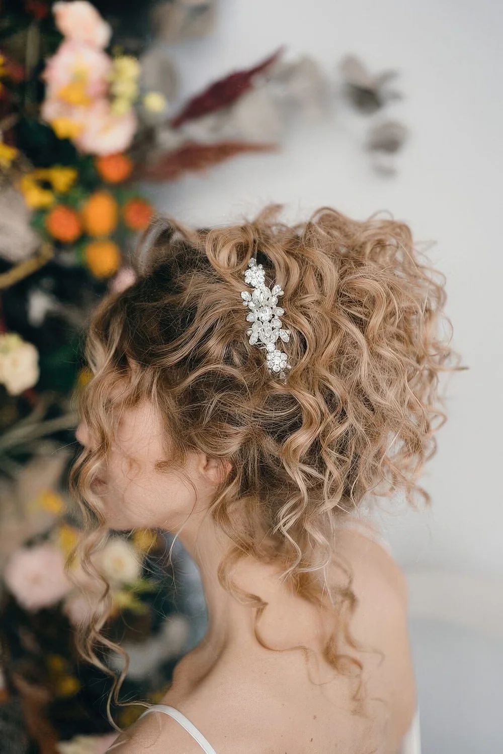 Relaxed curly updo with some curls down and an elegant rhinestone hairpiece on one side.