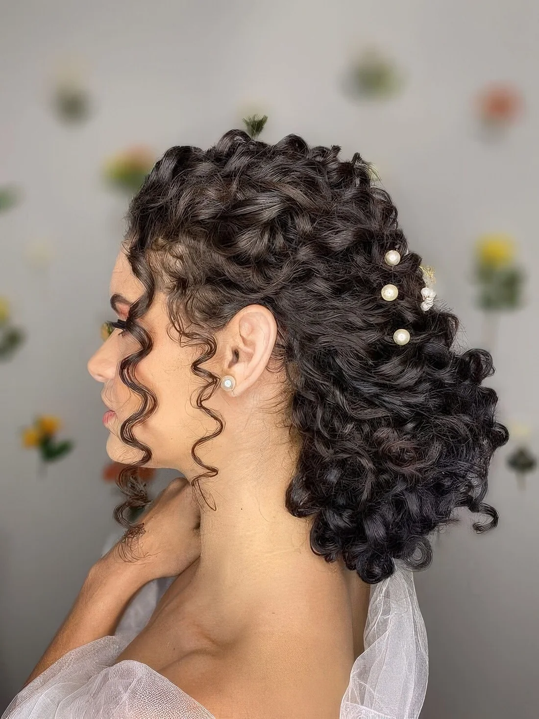 Low curly wedding updo with a curly top, a large low bun and curls to highlight the face plus pearl hair pins.