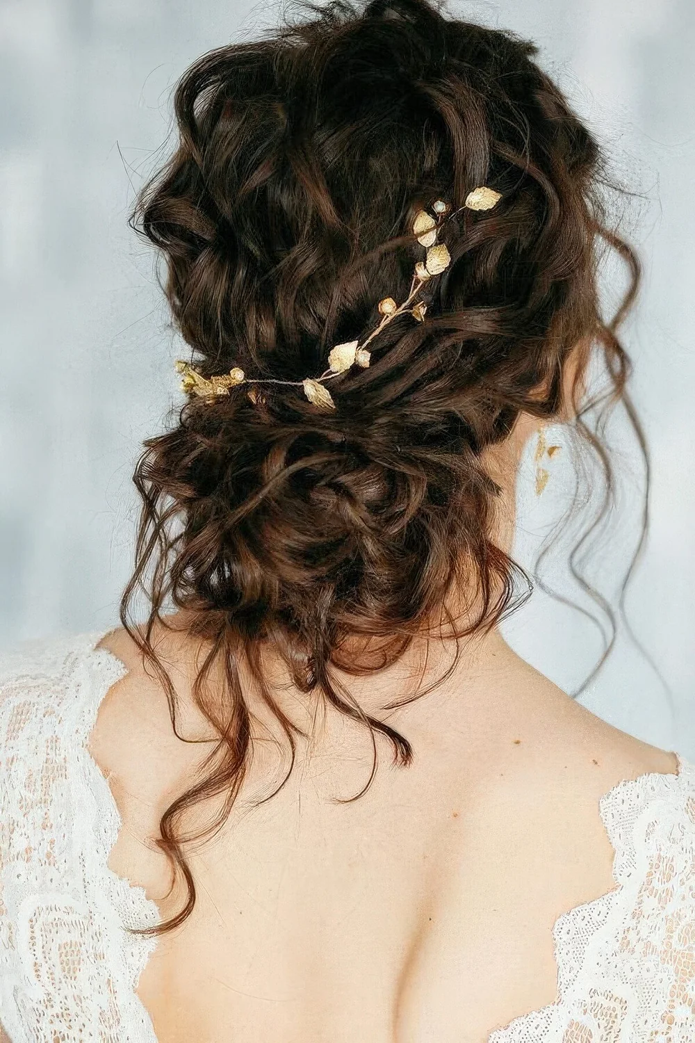 Messy curly low bun with a curly top and a chic gold leaf hair vine plus some curls down.