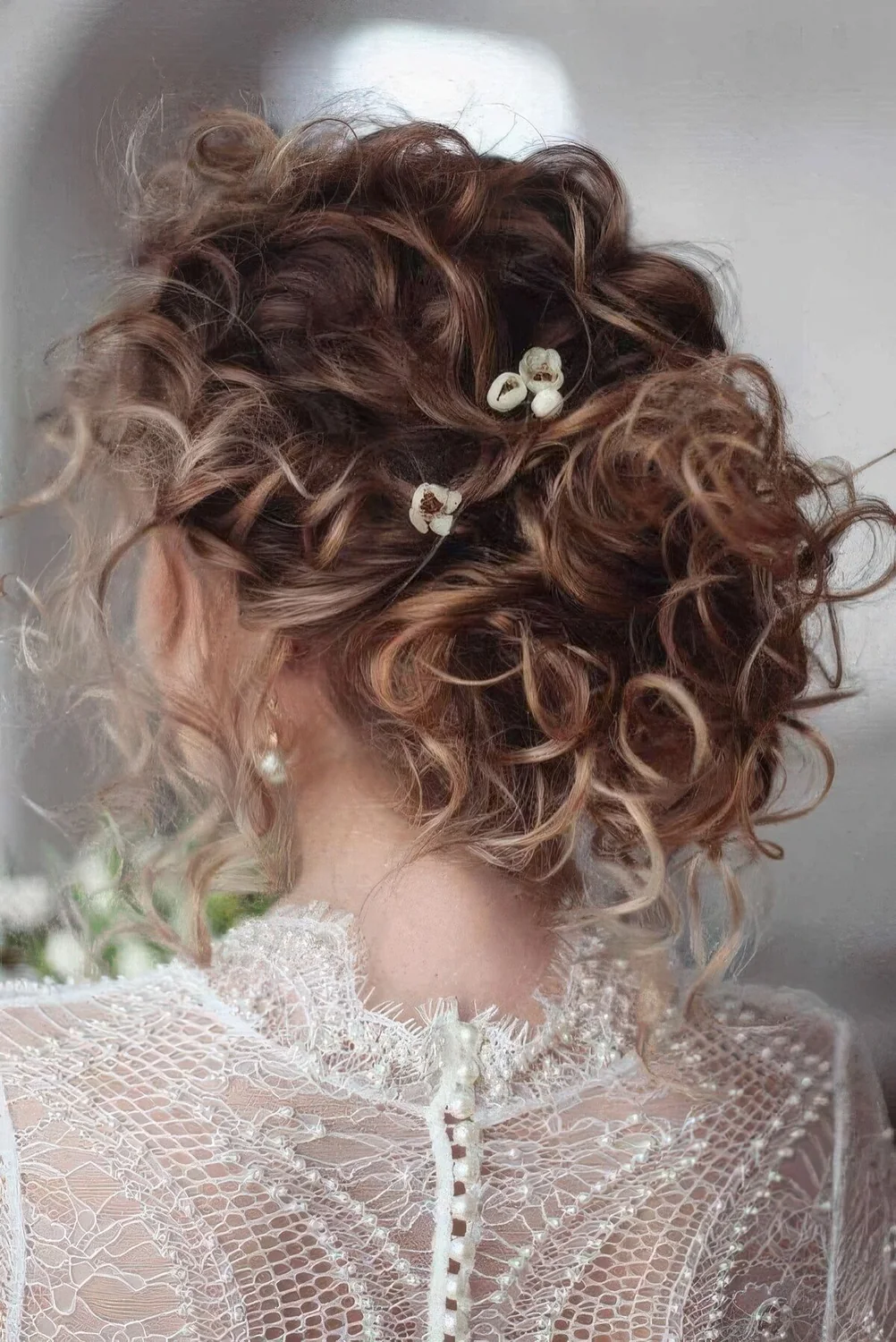 Messy curly updo on medium hair, with messy curls all over and some blooms.