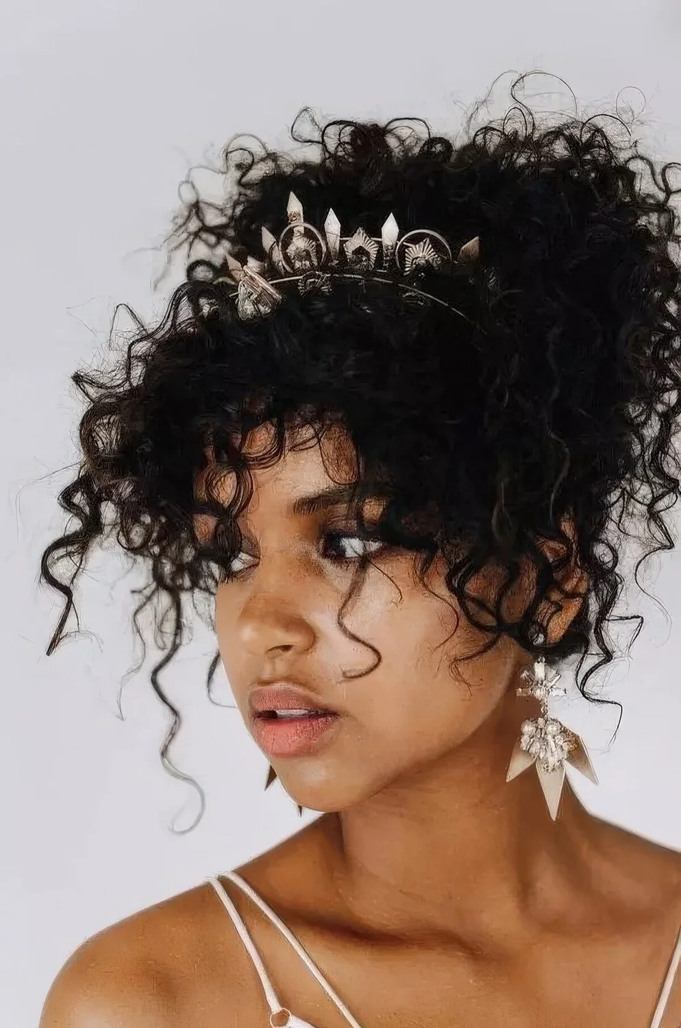 Natural curls styled into an updo with many locks down accented with a trendy crystal headpiece.