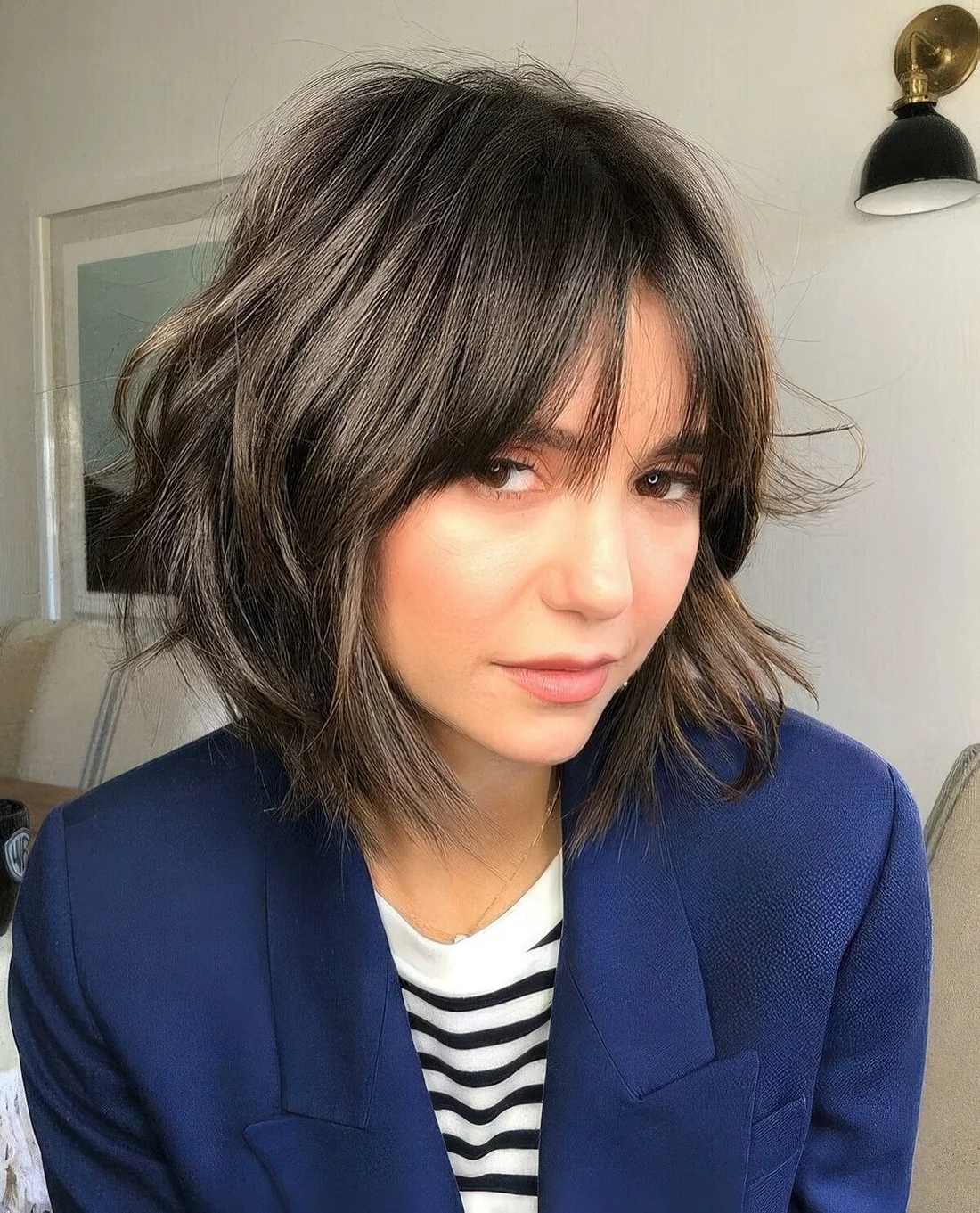 Dark brown chin-length shaggy bob with wispy bangs.