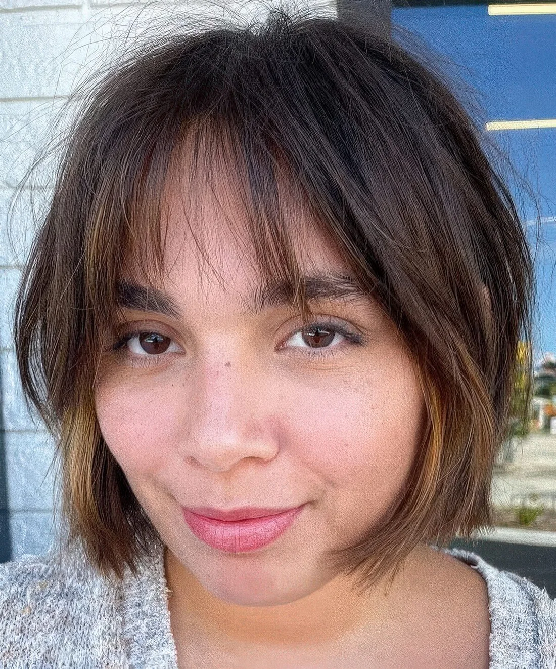 Dark brown jaw-length bob with caramel balayage and wispy bangs.