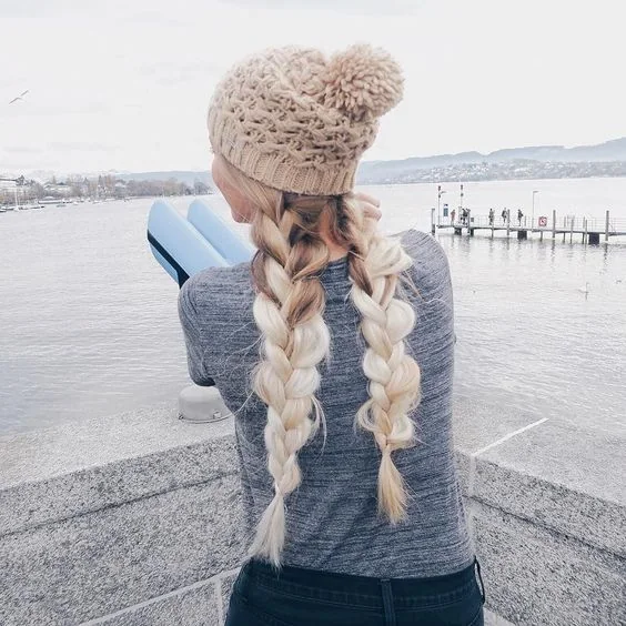 Two voluminous braids with a neutral beanie.