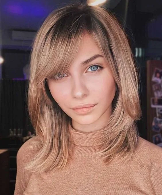 Honey blonde medium-length hair with side bangs.