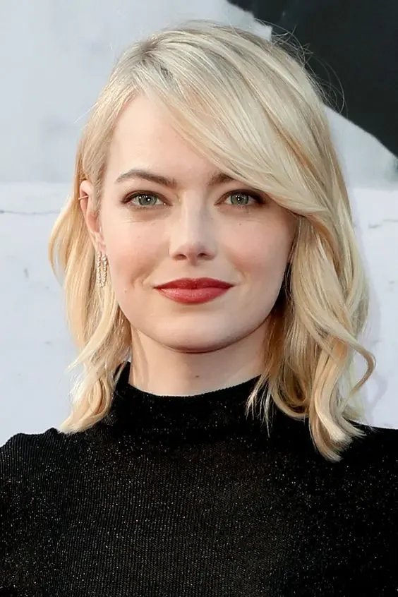 Emma Stone wearing creamy blonde medium-length hair with side bangs.