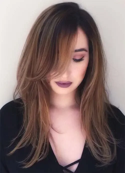 Long layered hair with dark root and light brunette highlights and side bangs.