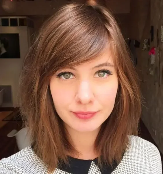 Medium-length auburn hair with side swept bangs.
