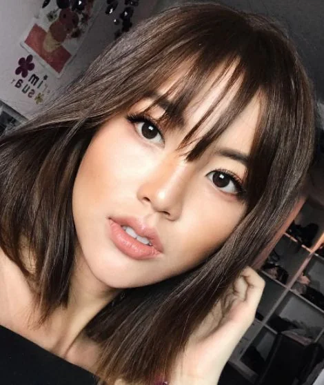 Shiny dark chestnut medium-length hair with wispy bangs.