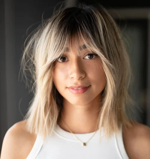 Blonde hair with a darker root and texture plus outgrown looking wispy bangs for a delicate touch.