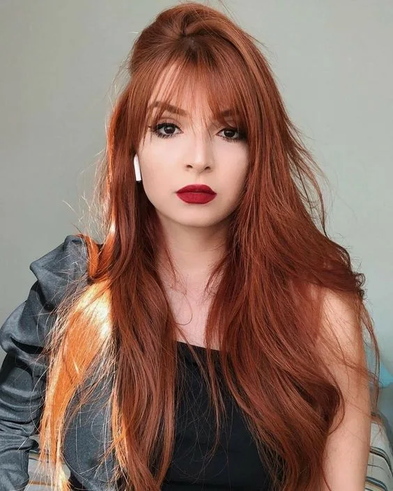 Long red hair with wispy bangs for subtle face-framing and to make a delicate touch with this hair color.