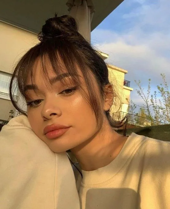 Dark brown hair in a top knot, with long wispy bangs for a delicate and pretty look.