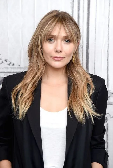Elizabeth Olsen wearing long blonde hair with caramel balayage and long wispy bangs for a touch of cute.