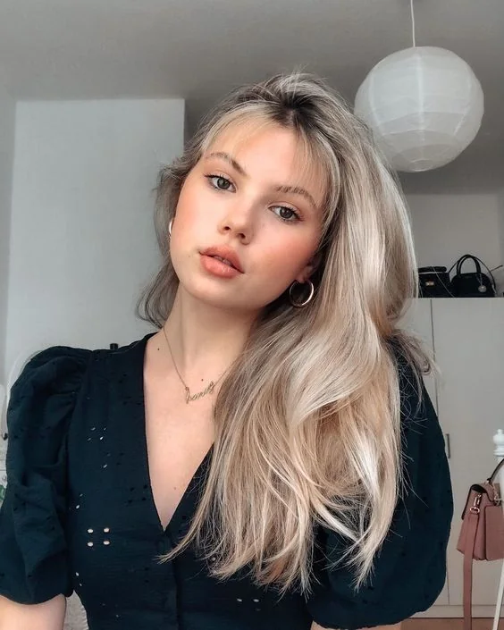 Long icy blonde hair with balayage of a warmer tone, a dark root and wispy bangs for a delicat elook.