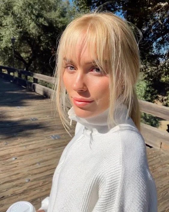 Long blonde hair in a low ponytail and with layered bangs including curtain and whispy ones for a more modern look.