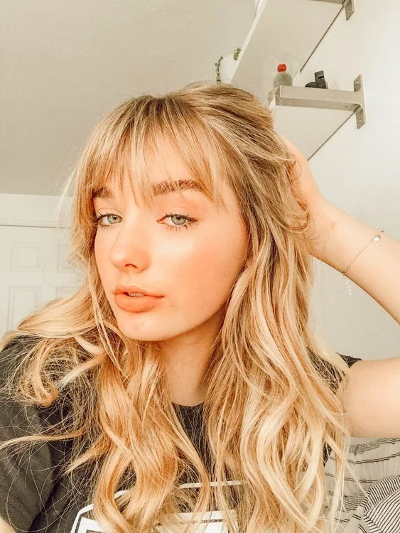 Long blonde wavy hair with delicate wispy bangs for beautiful face-framing and for a girlish look.