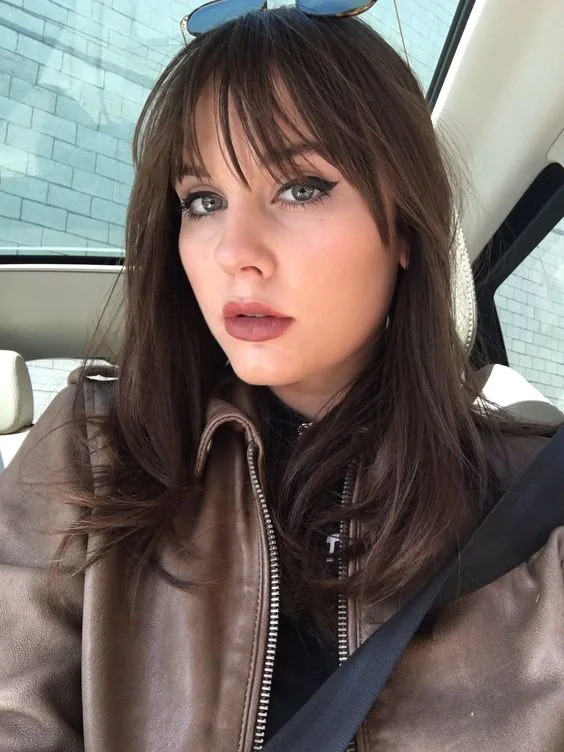 Long dark brown hair with layered bangs curtain and wispy ones to frame the face in a stylish way.