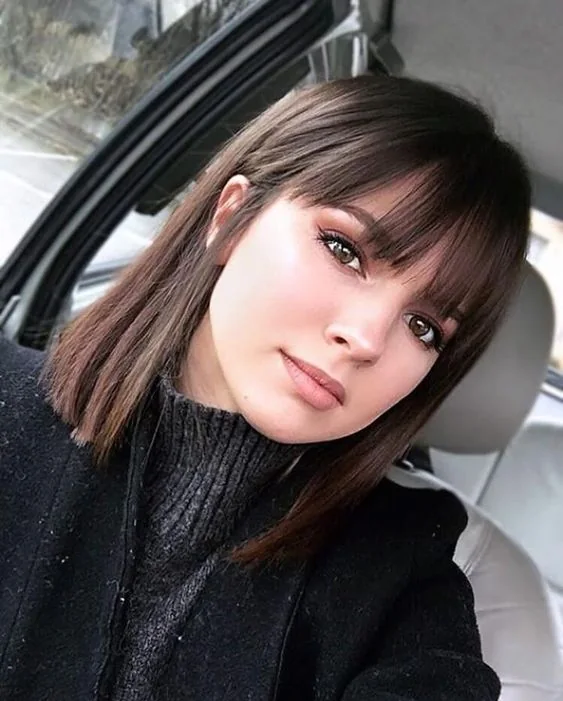 Medium-length dark brown hair with wispy bangs.