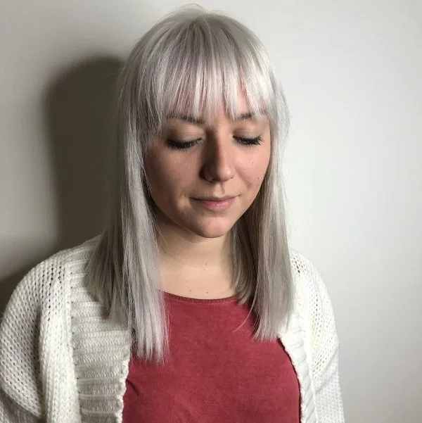 Silver blonde medium-length hair with wispy bangs that look harsh and make a statement with such a hair color.
