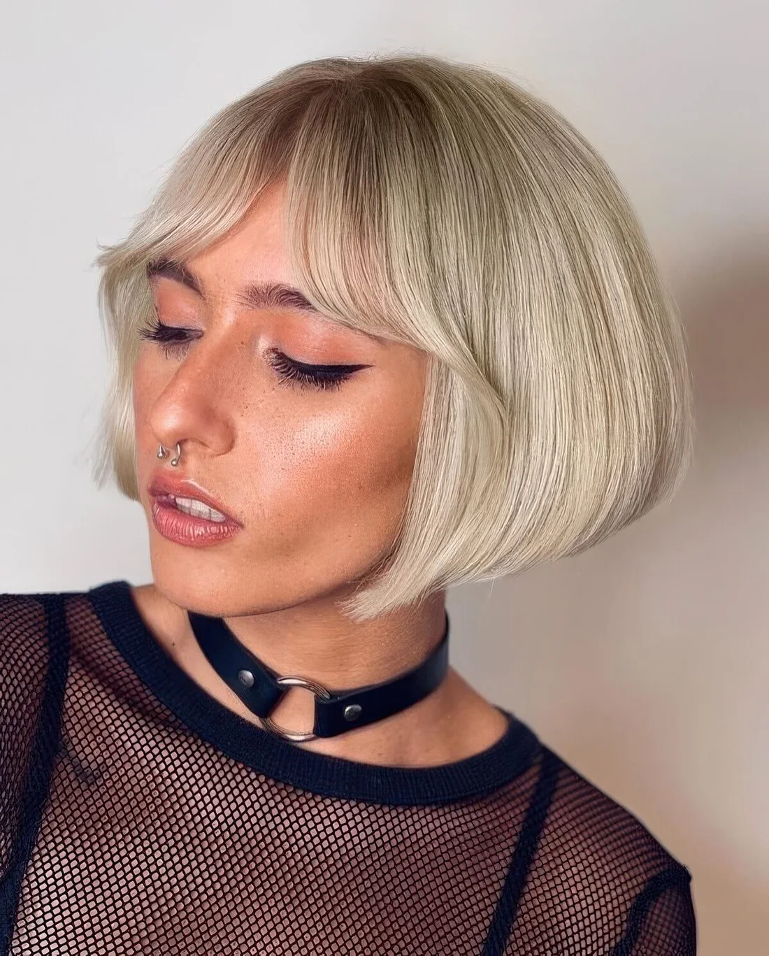 Sleek blonde angled ear-length bob with curtain bangs.