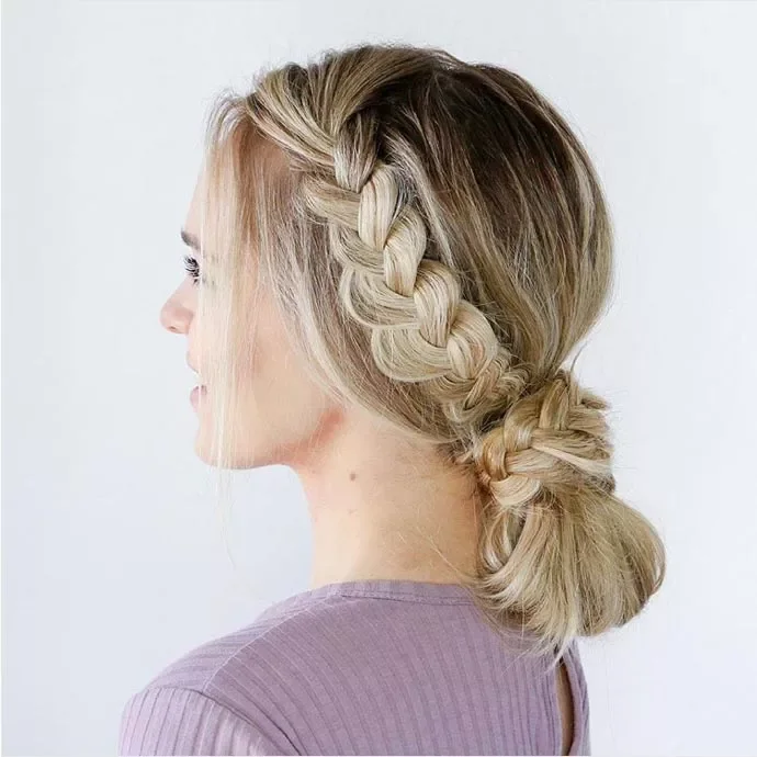 Side view of a blonde French braid gathered into a low textured bun