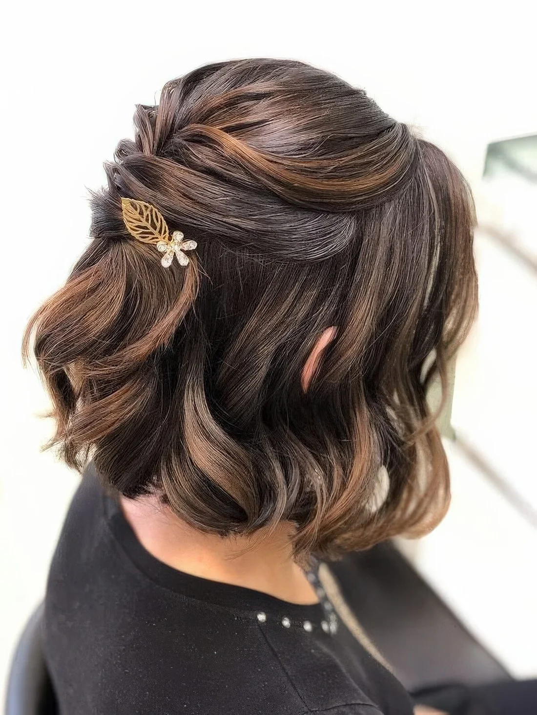 Refined half updo on medium-length hair with twists and waves down, a little leaf and flower hair pin and face-framing locks.