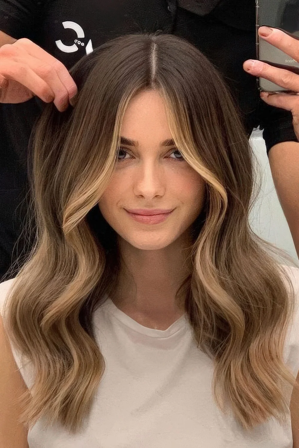 Long brunette hair with blonde balayage and face-framing highlights, with volume and waves.