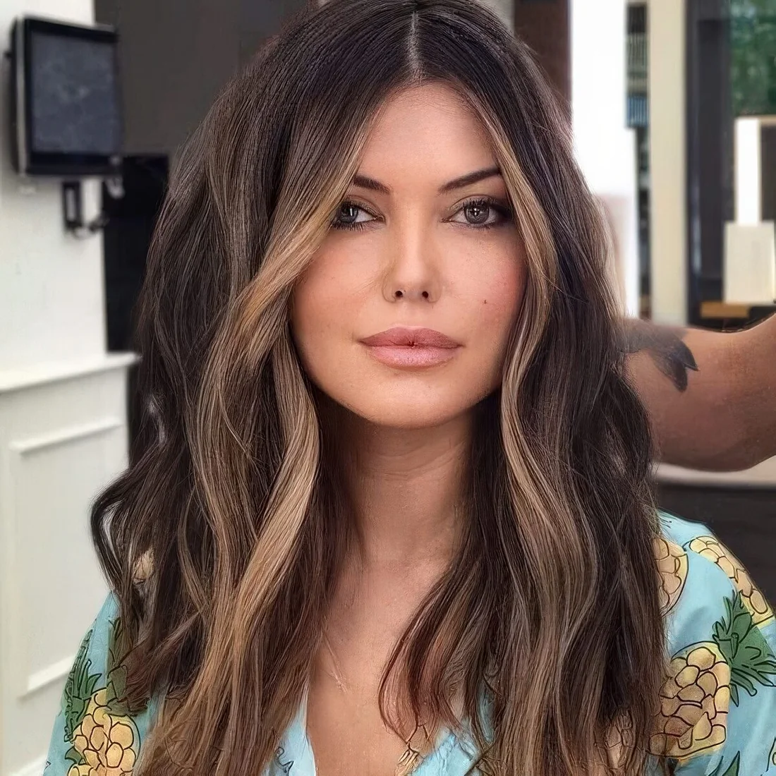 Long wavy brunette hair with slim blonde face-framing highlights.