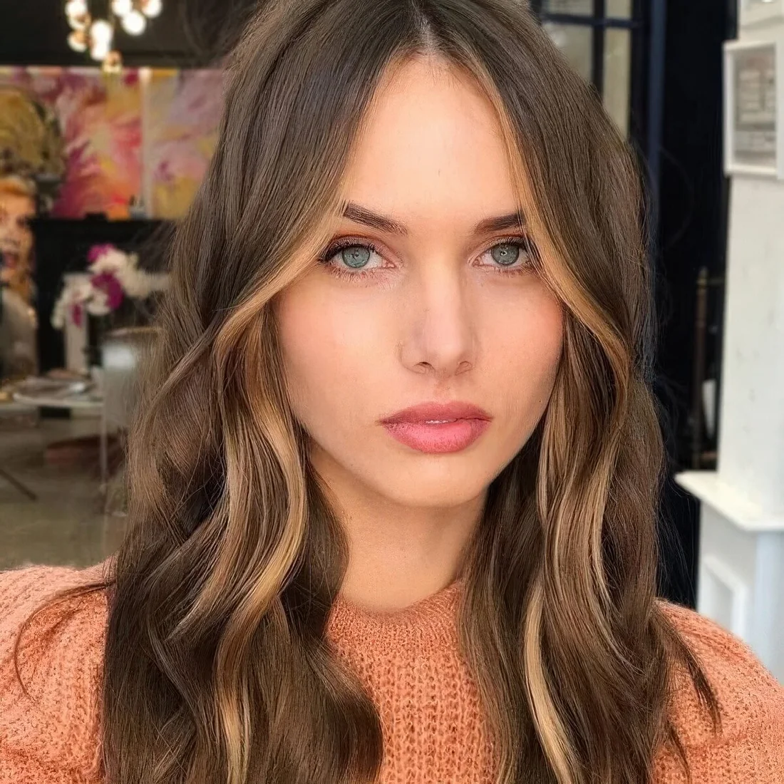 Long dark brunette hair with caramel face-framing highlights, waves and a bit of volume.