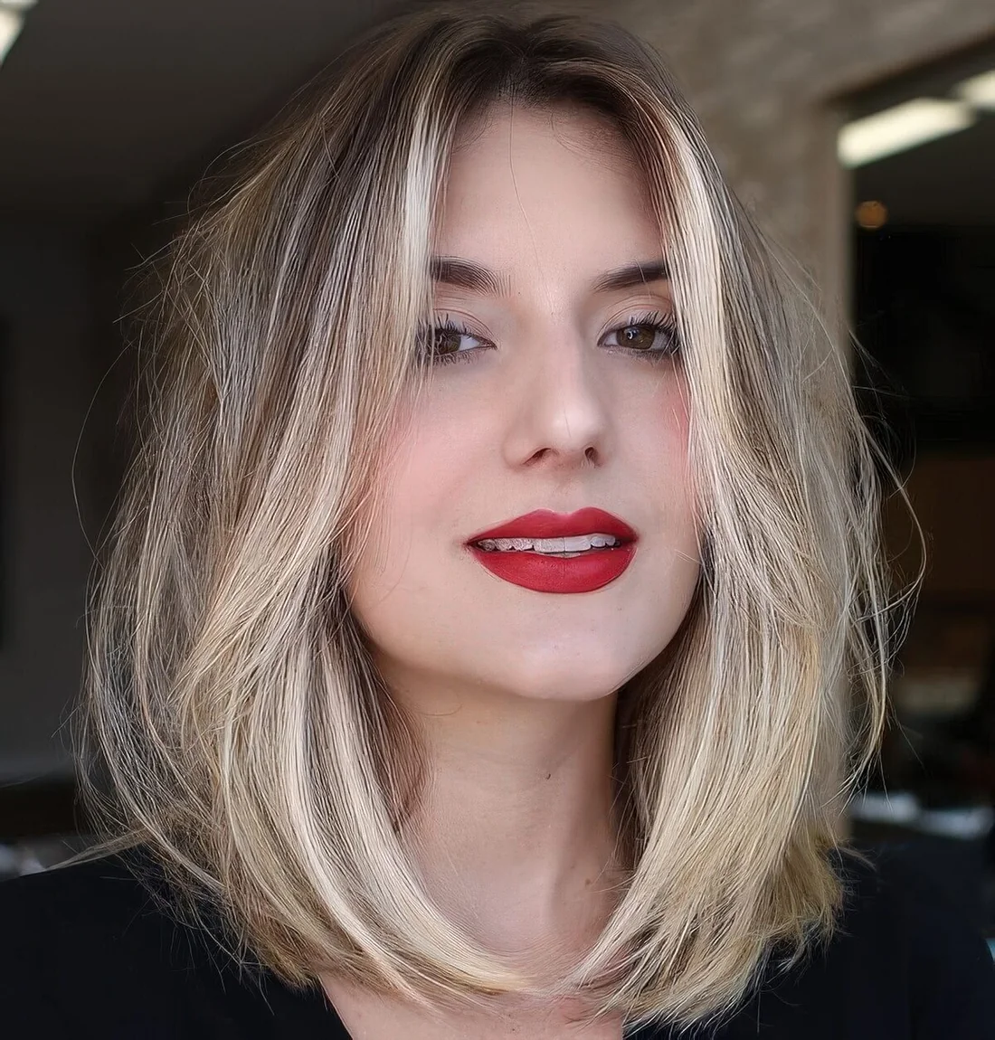 Blonde medium-length haircut with a darker root and face-framing layers.