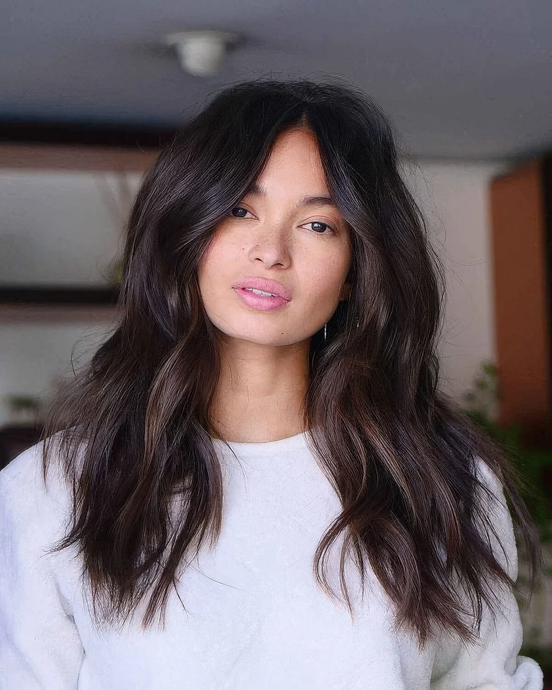 Long dark brunette hair with center part and layers including face-framing ones, with delicate balayage.