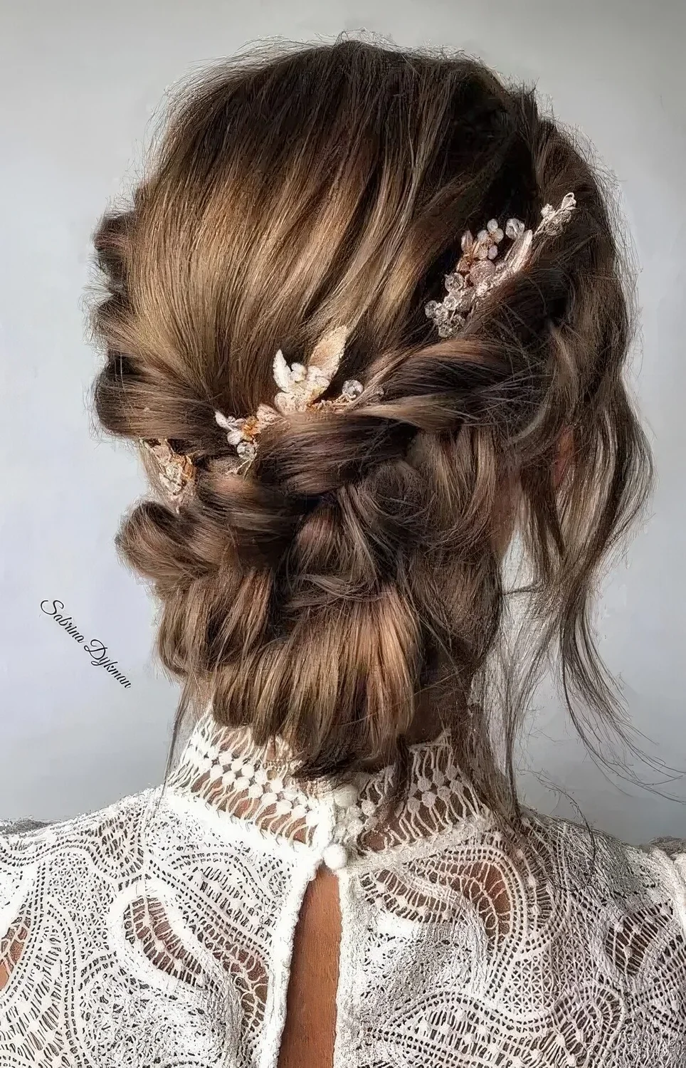 Braided low updo with two side braids, a bump, a low bun and face-framing locks plus some beaded hair pieces.