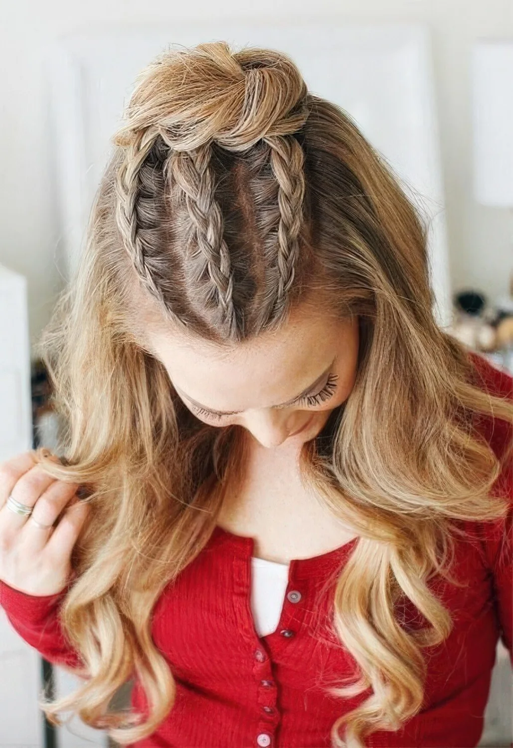 Very creative half updo with three French braids on top and a top knot, waves down.
