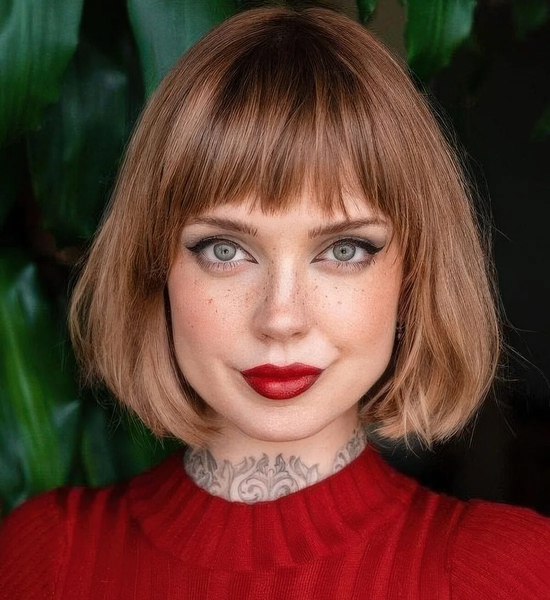 Brown reddish chin-length bob with blunt textured bangs and curved ends.