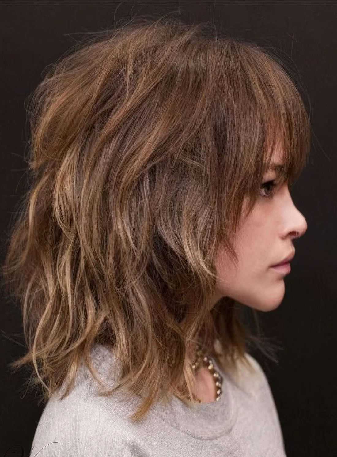 Shoulder-length layered shaggy haircut with blonde highlights and overgrown bangs.