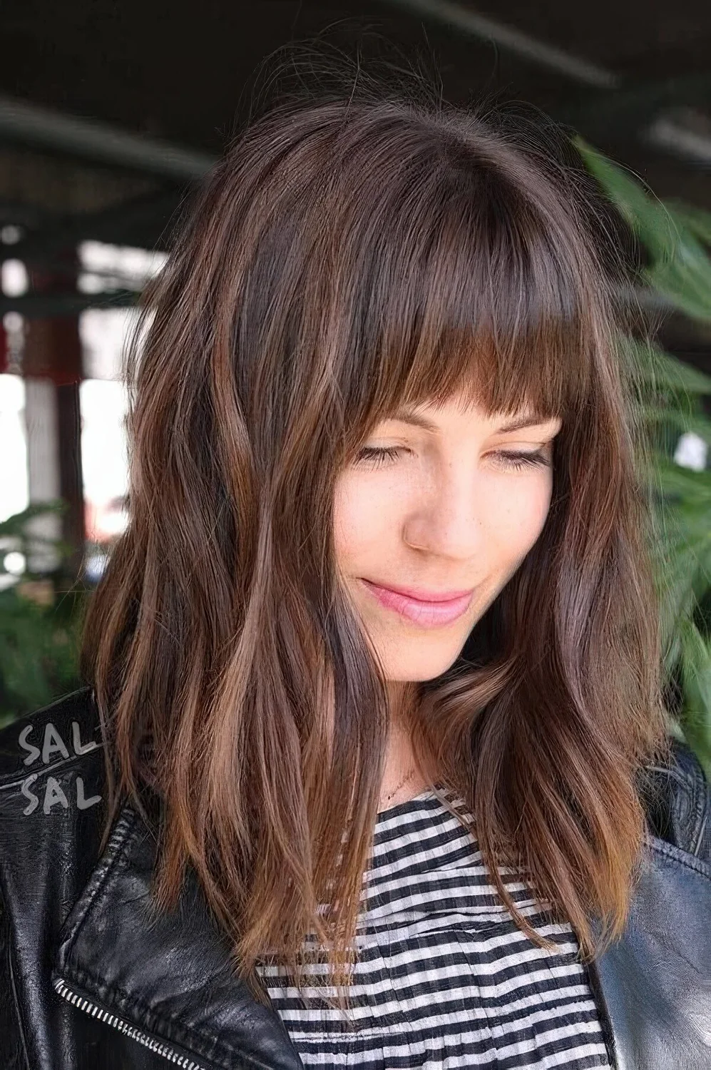Dark brown hair with a lighter chestnut balayage, messy waves and Birkin bangs wispy ones.