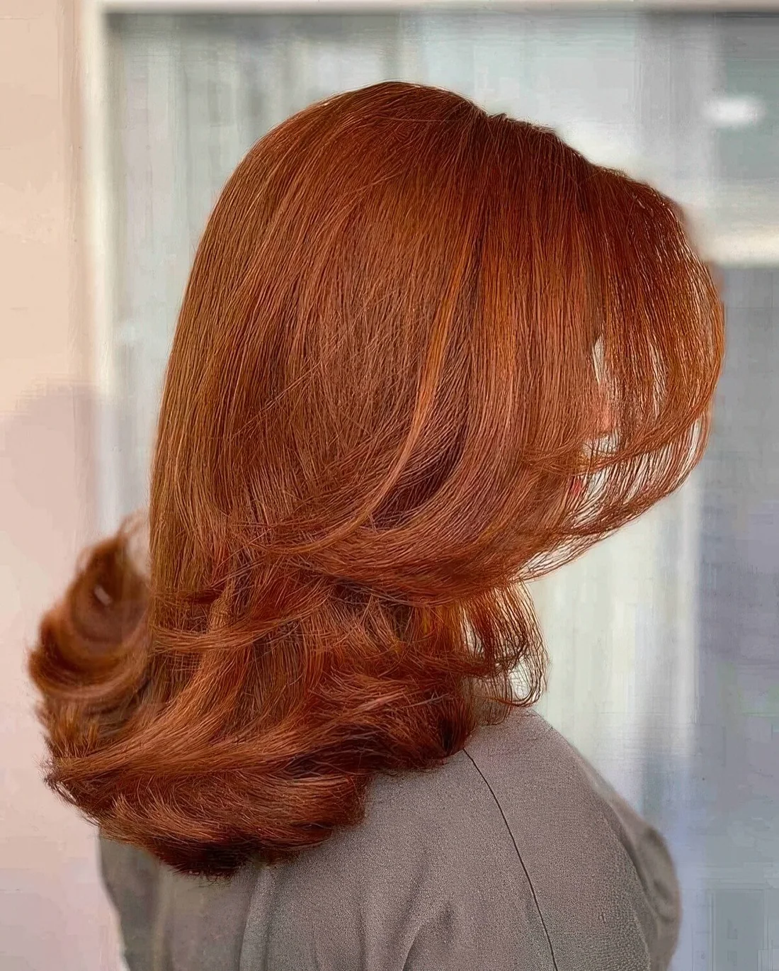 Bright copper butterfly haircut on medium-length hair, with curled ends.