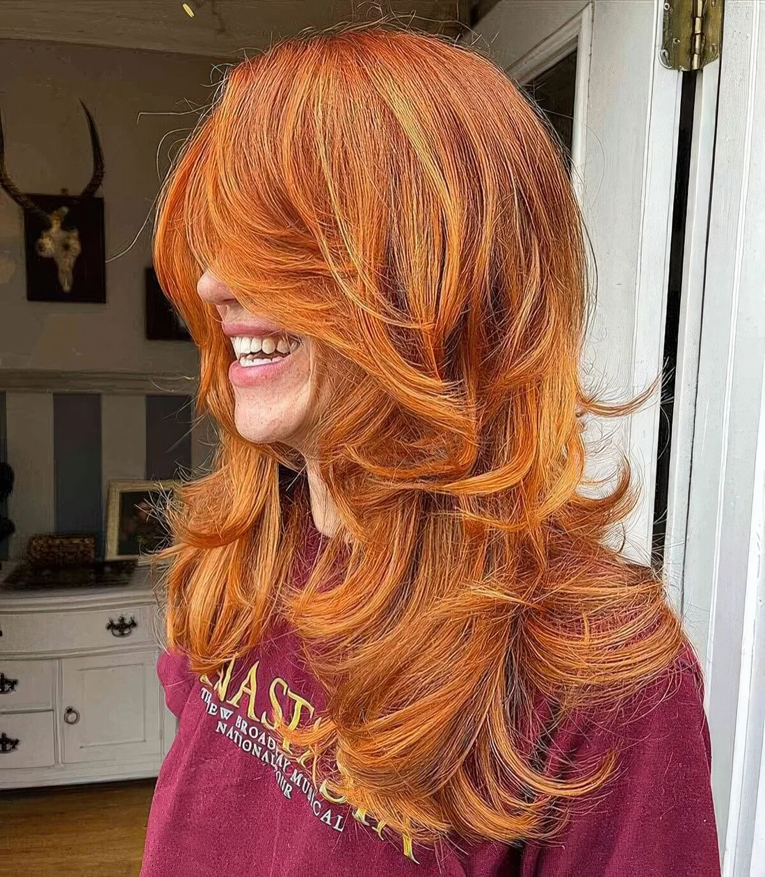 Copper voluminous butterfly haircut on long hair, with blonde highlights and curled ends.
