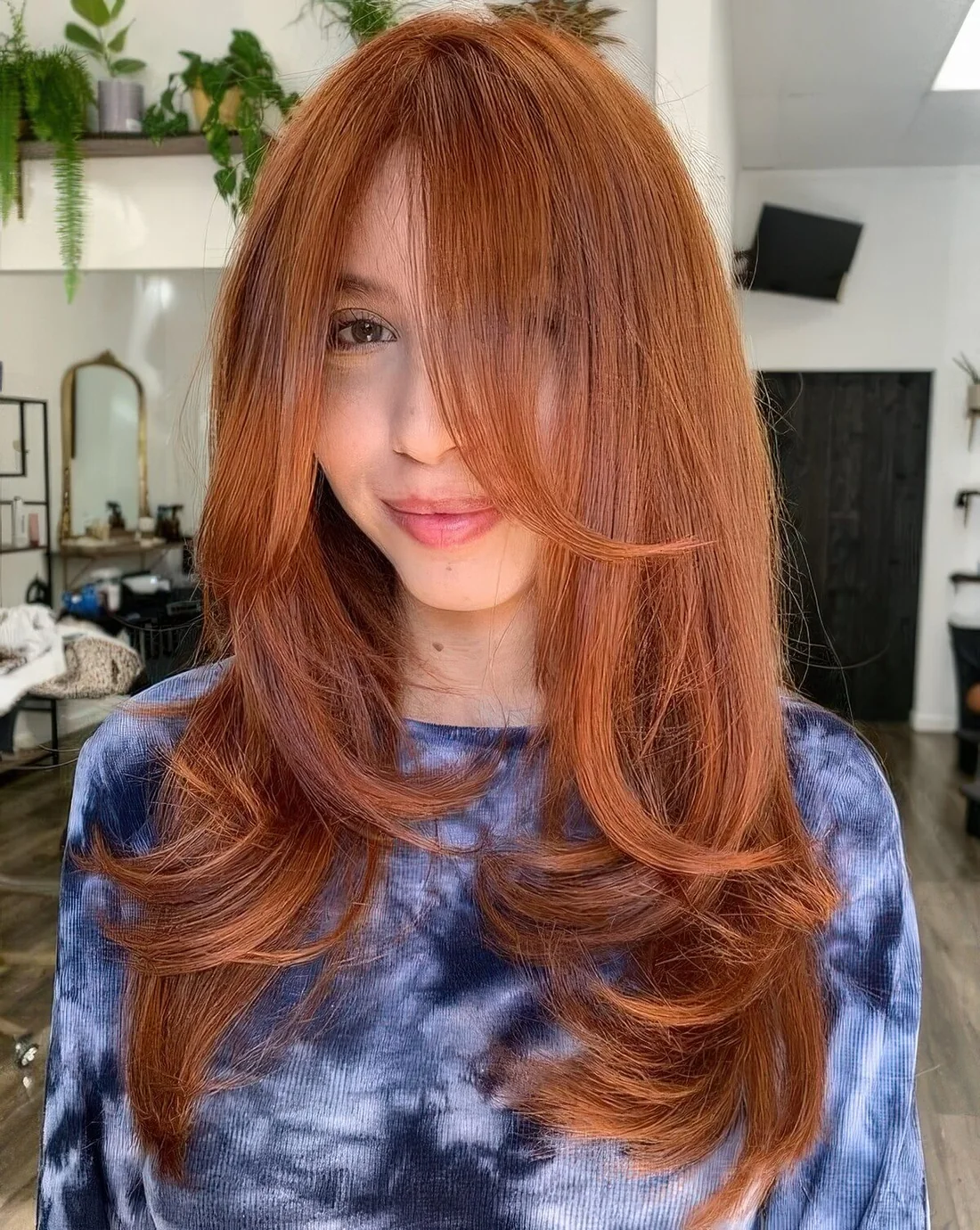 Long and beautiful ginger butterfly haircut with curled ends and bottleneck bangs.