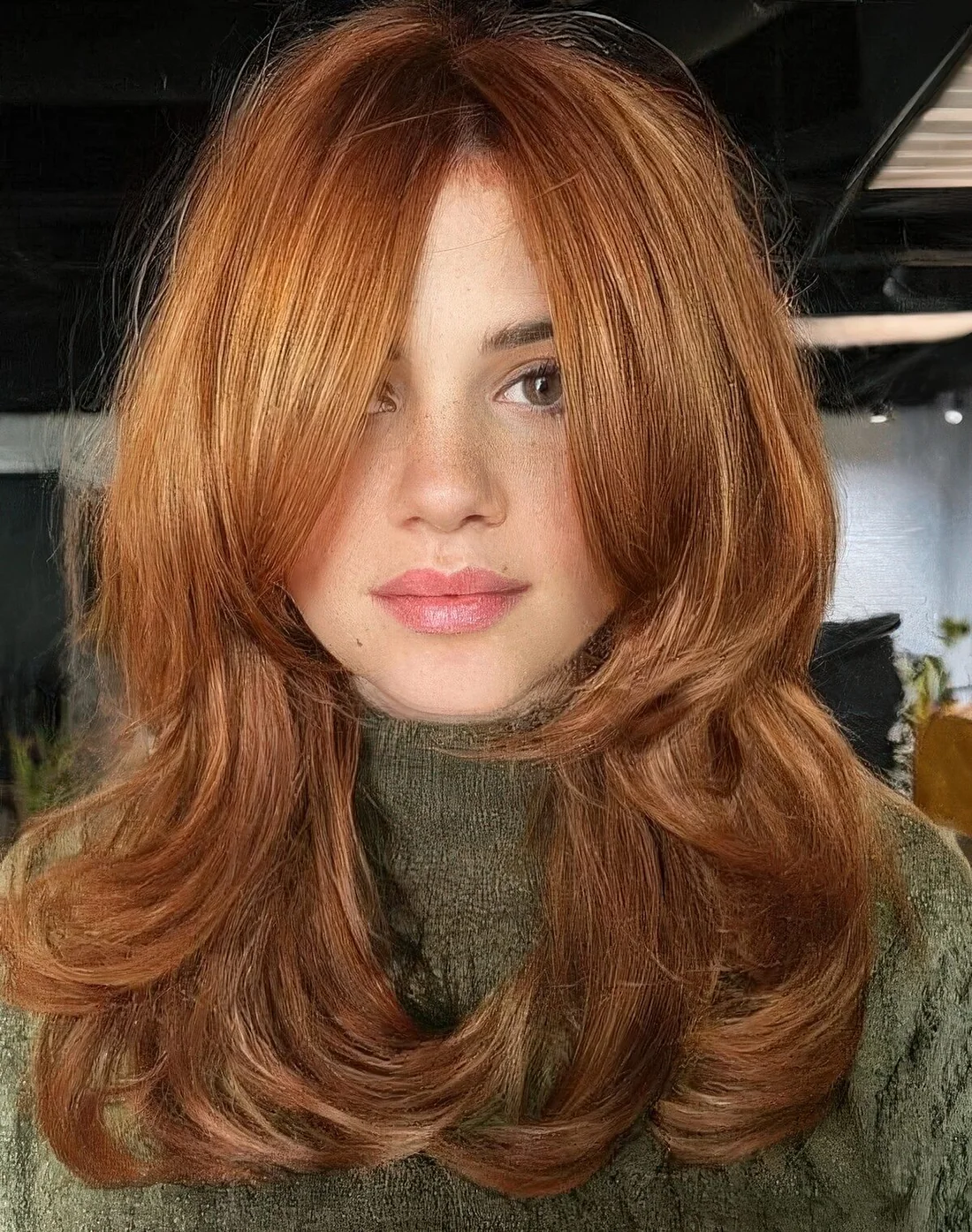 Medium ginger butterfly haircut with bottleneck bangs and curled ends.