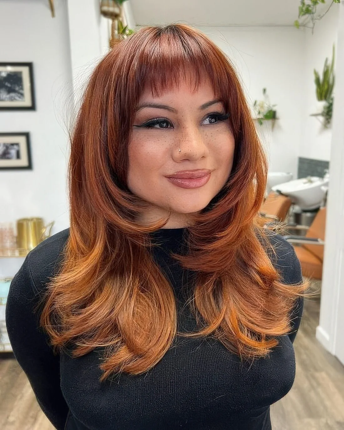 Red to giner butterfly haircut with baby wispy bangs and a lot of volume, an ombre effect.