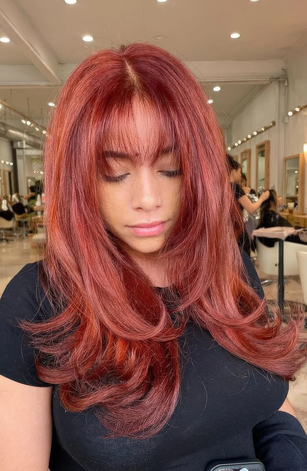 Extra bold red butterfly haircut with face-framing layers and wispy bangs, volume and curled ends.