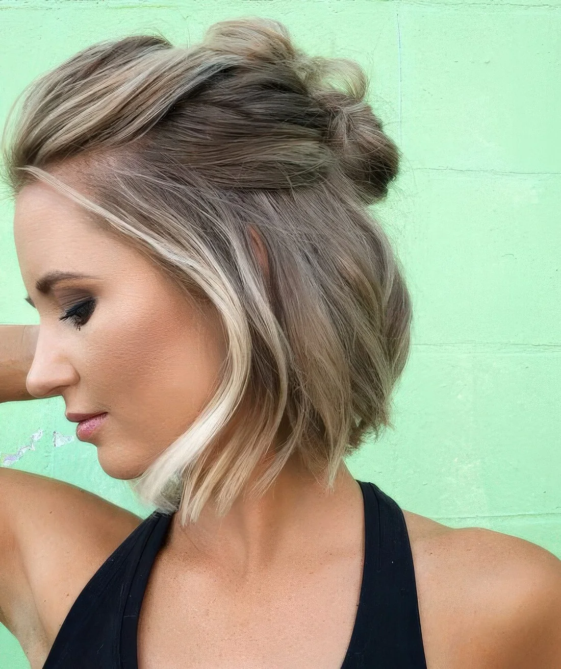 Chin-length bob styled as a half updo with some knots and a bump on top and textured hair down.
