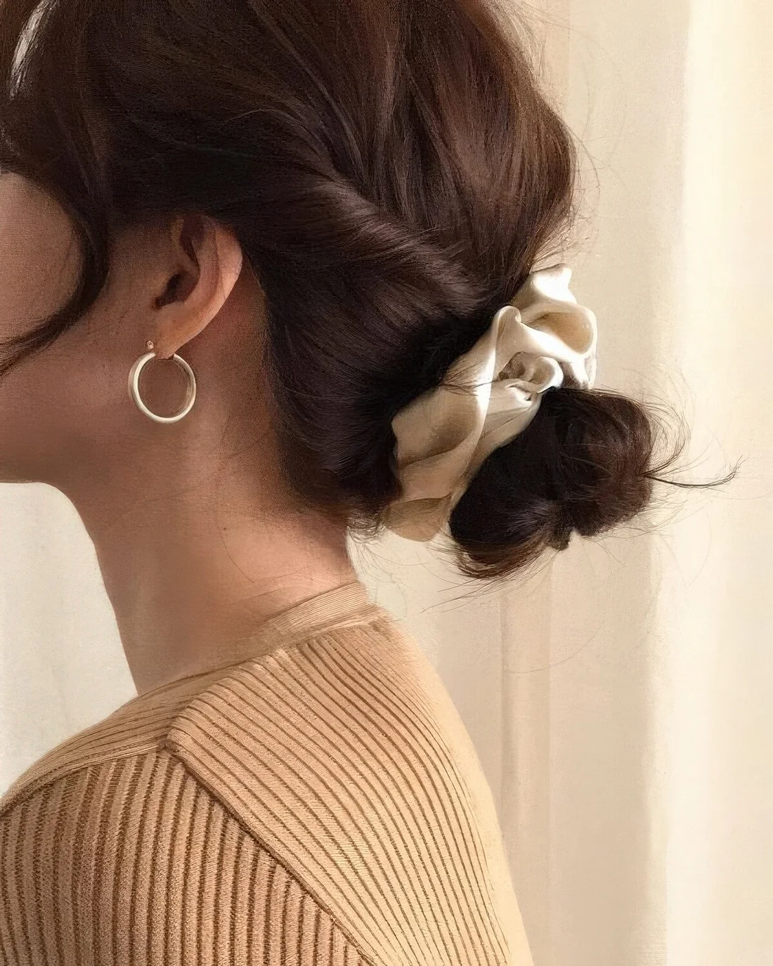 Low bun with twisted hair and face-framing bangs plus a scrunchie.