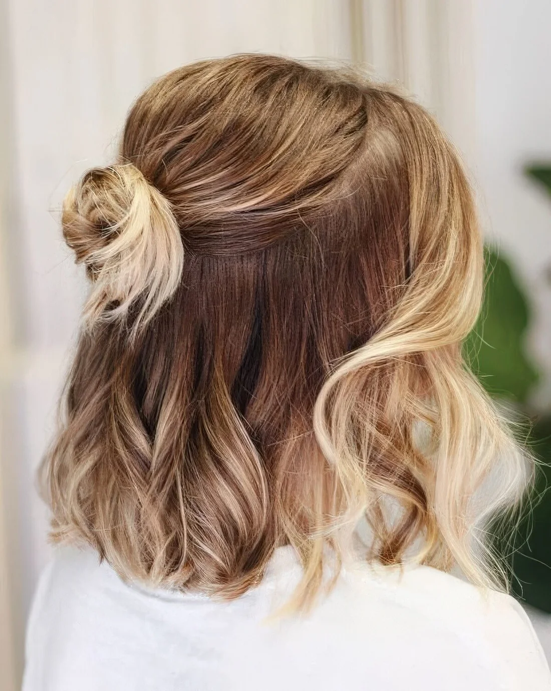 Medium hair half updo with a bump on top, a small bun and waves down plus face-framing hair.