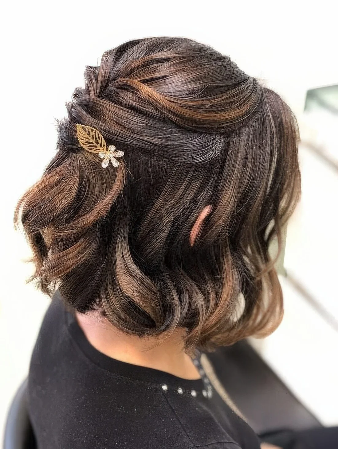 Refined half updo on medium-length hair with twists and waves down, a little leaf and flower hair pin and face-framing locks.